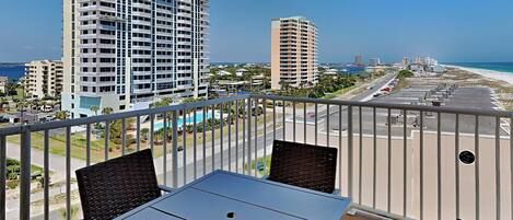 A balcony with a table and chairs, overlooking a beach and high-rise buildings.
