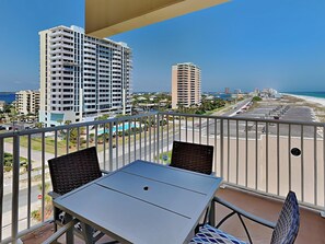 Un balcon avec une table et des chaises, donnant sur une plage et des immeubles de grande hauteur.