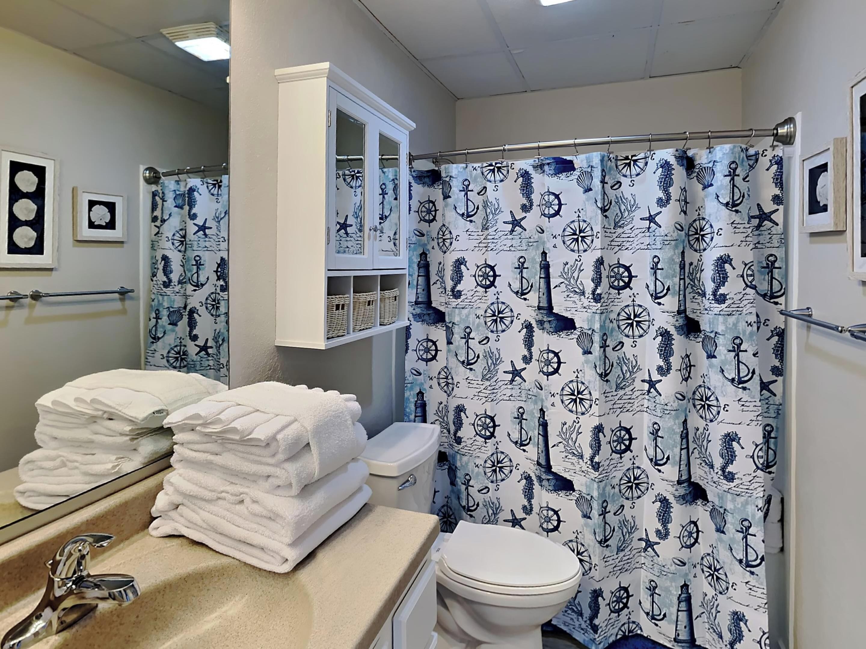 A bathroom with a nautical-themed shower curtain, a sink with a mirror, and a toilet.