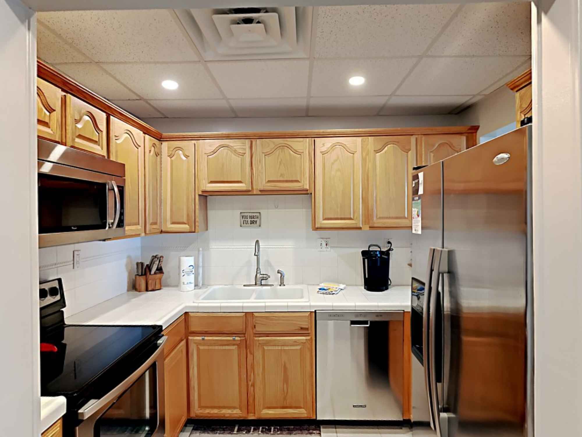 Una cocina compacta con muebles de madera, microondas, lavavajillas y refrigerador.