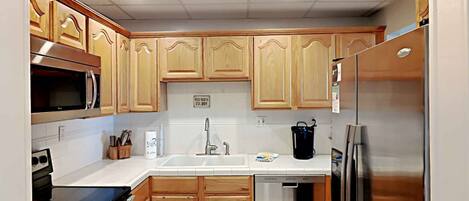 Una cocina compacta con muebles de madera, microondas, lavavajillas y refrigerador.
