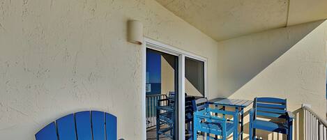 A balcony with blue chairs and a table, a sliding glass door, and a textured wall.