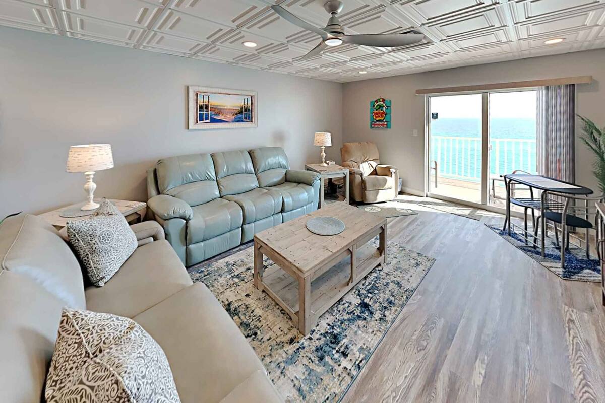 A spacious living room with a sofa, coffee table, and a view of the ocean through a large sliding glass door.