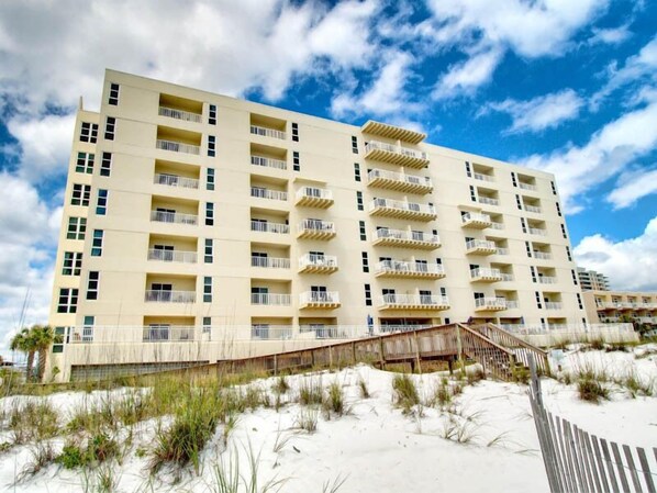 Un hôtel à plusieurs étages, doté de balcons, situé près d’une plage de sable et agrémenté d’une promenade en bois.