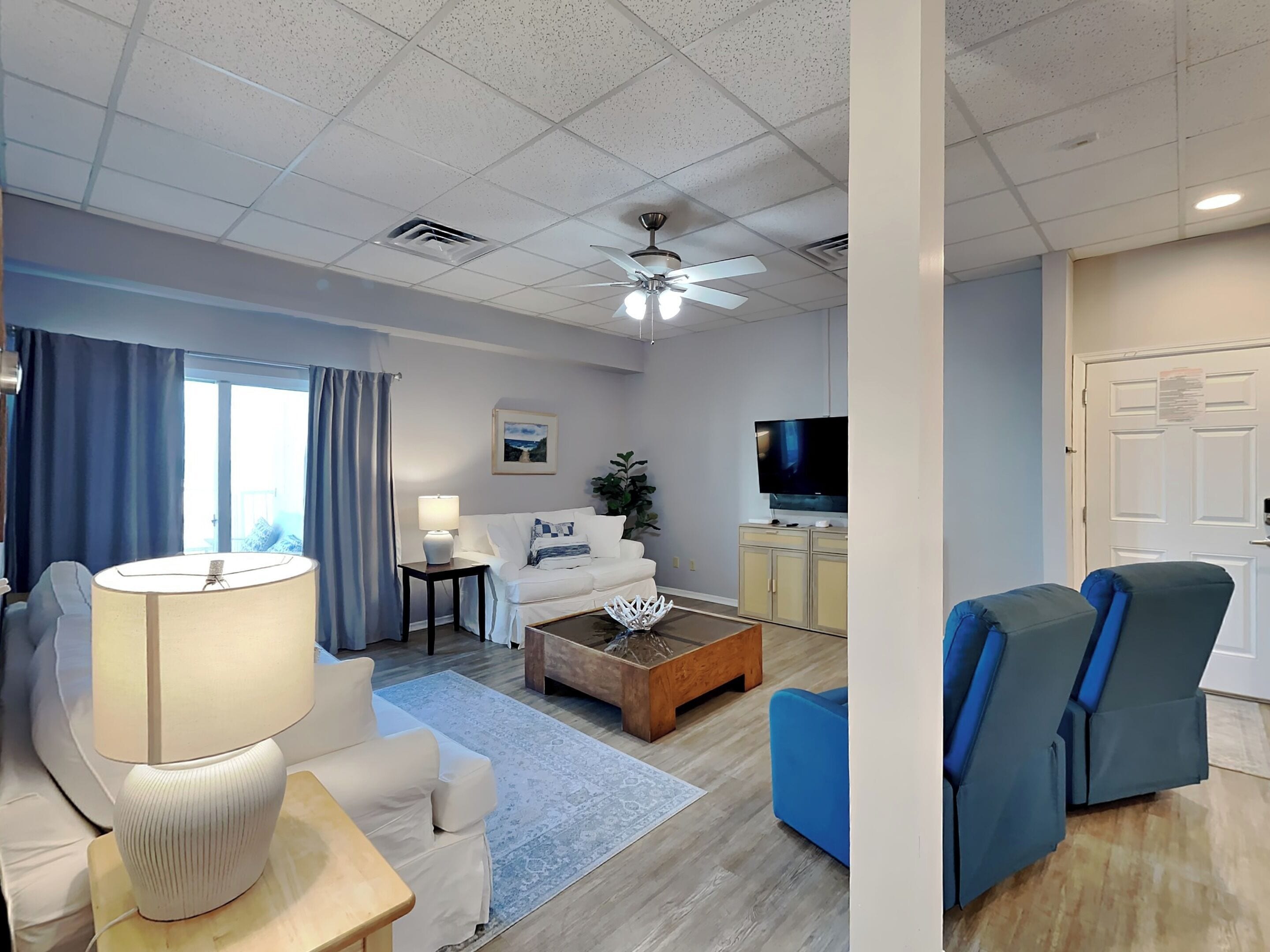 Un salon moderne avec un canapé blanc, une table basse, un téléviseur et un ventilateur de plafond.
