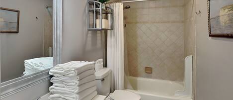 A bathroom with a sink, toilet, and bathtub. There is a towel rack with folded towels, a mirror, and a framed picture on the wall.