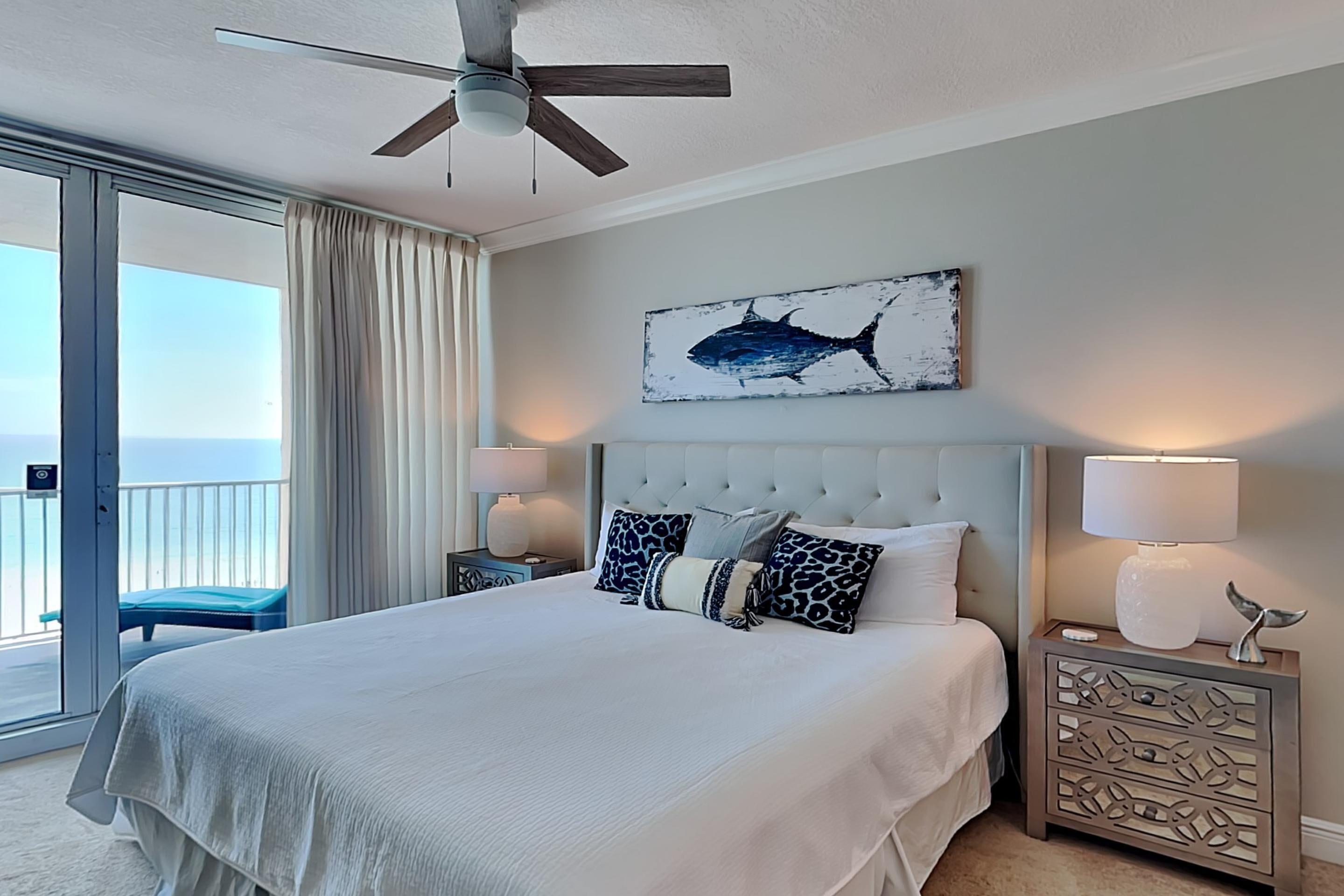 Hotelkamer met een groot bed, een plafondventilator, een balkon met uitzicht en een kunstwerk met haaien op de muur.