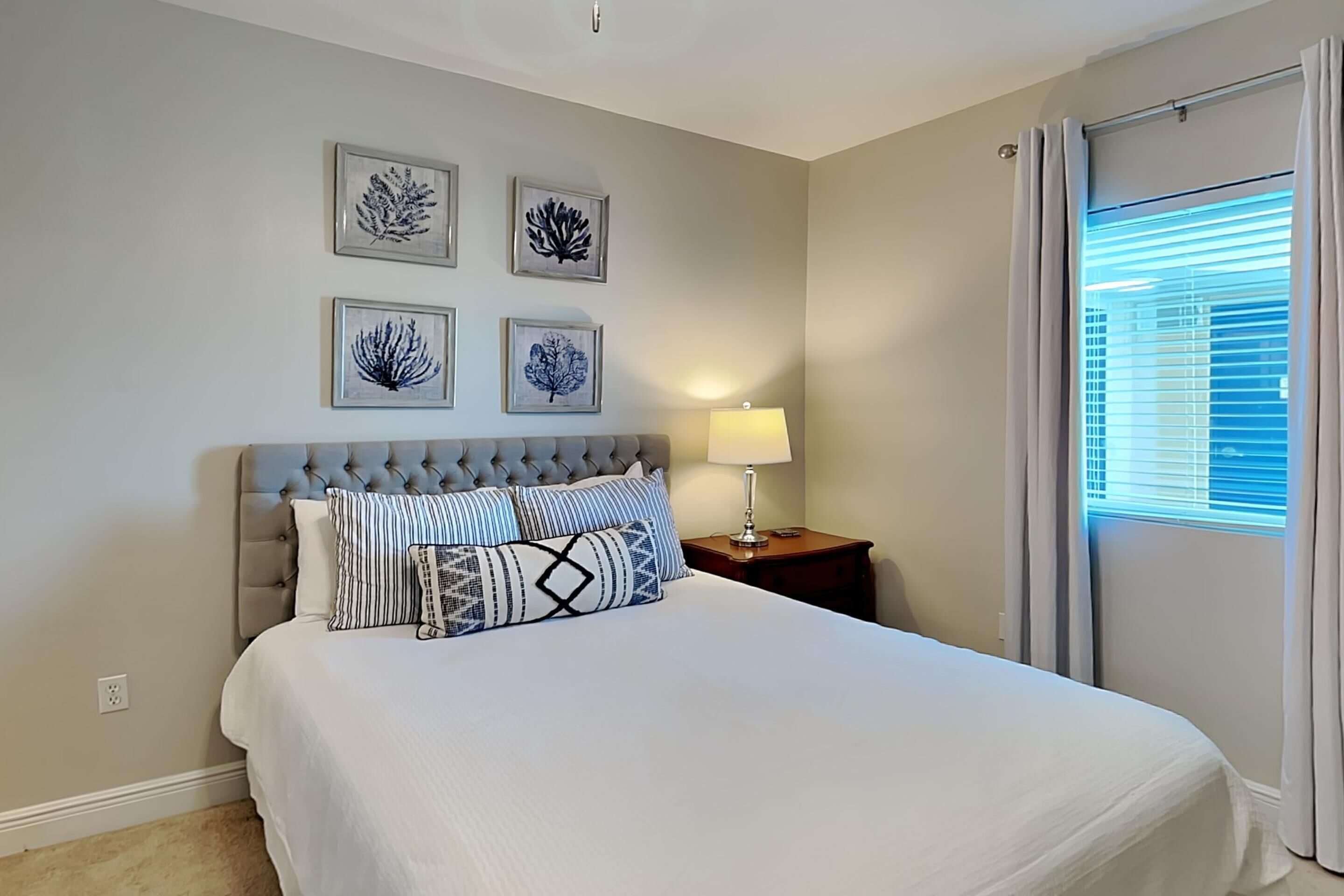 A bedroom with a large bed, a nightstand, a lamp, and framed artwork on the wall.