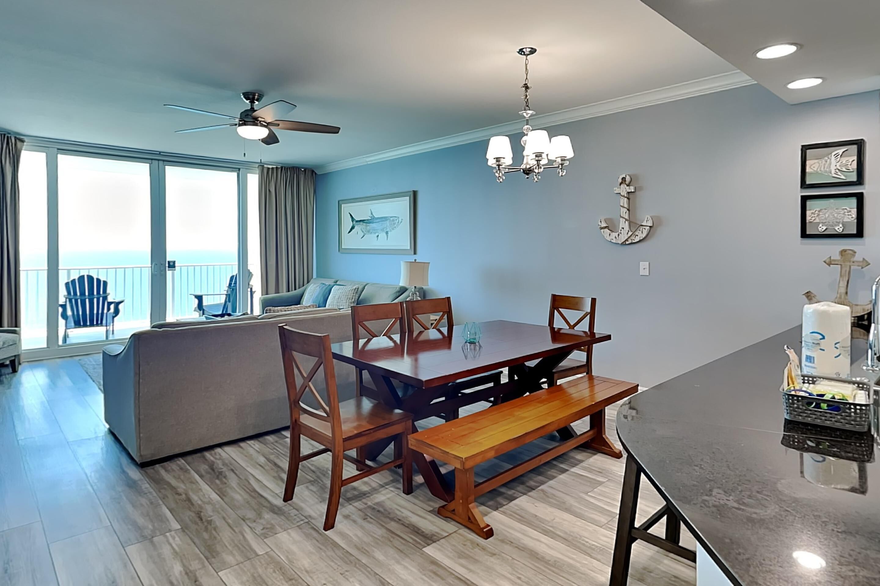 A spacious living area with a wooden dining table, a sofa, and a balcony with a view.