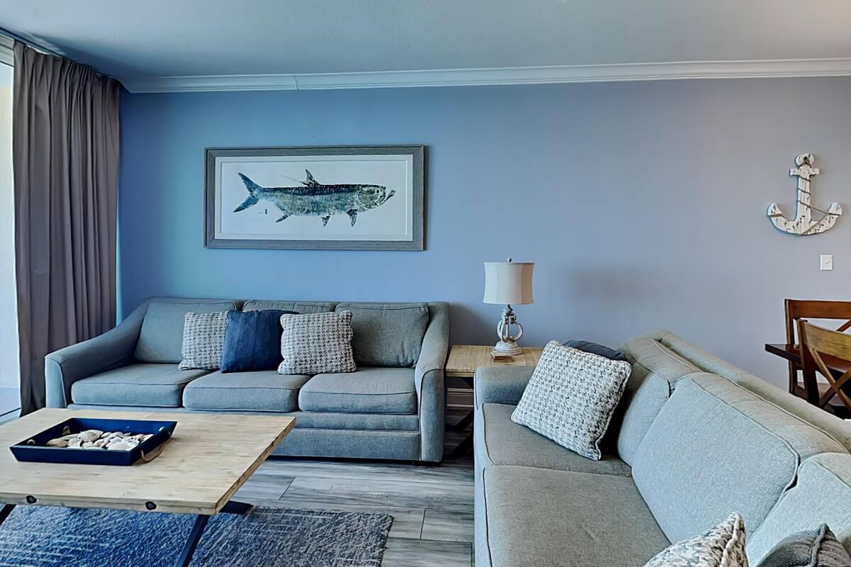 A living room with two grey sofas, a coffee table, a framed fish artwork, a lamp, and a wooden chair.