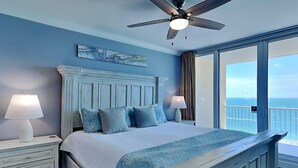 A bedroom with a large bed, two bedside tables with lamps, a ceiling fan, and a view of the ocean through a large window. - San Carlos by Southern Vacation Rentals (Gulf Shores)