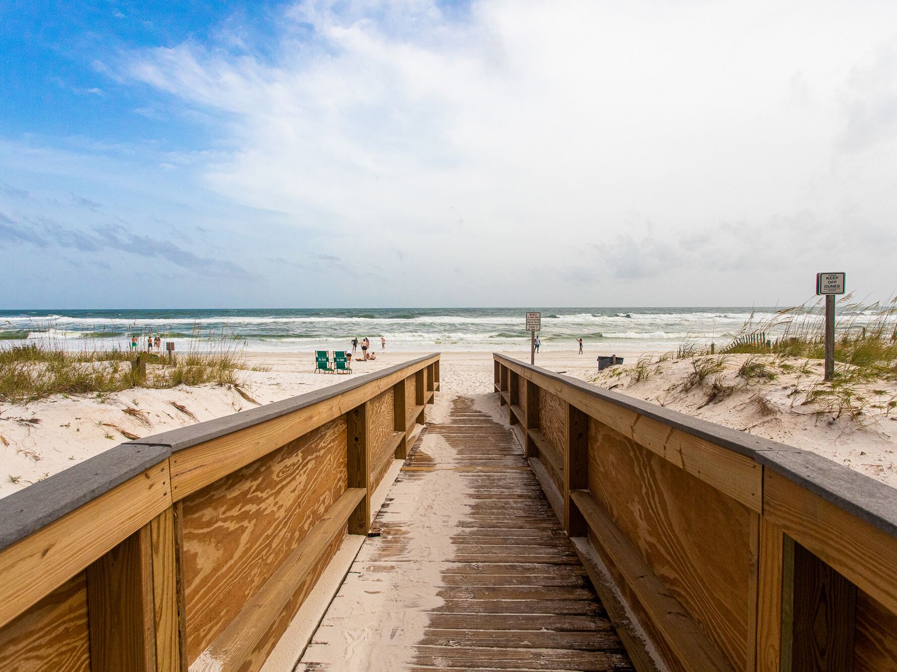 A wooden boardwalk leading to a beach with a sign that reads "KEEP OFF DUNES."