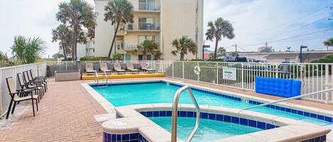 A swimming pool with a tiled edge, lounge chairs, and a building in the background.
