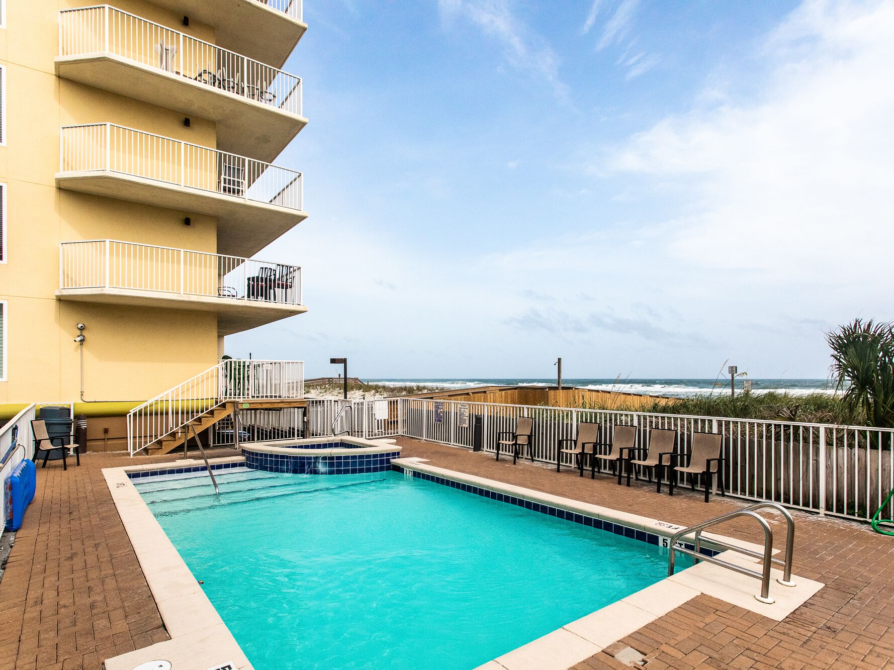 A swimming pool with a view of the ocean, a covered patio area, and a multi-story building with balconies.