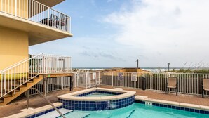 Uma área de piscina com hidromassagem, um deck de madeira e vista para a praia.