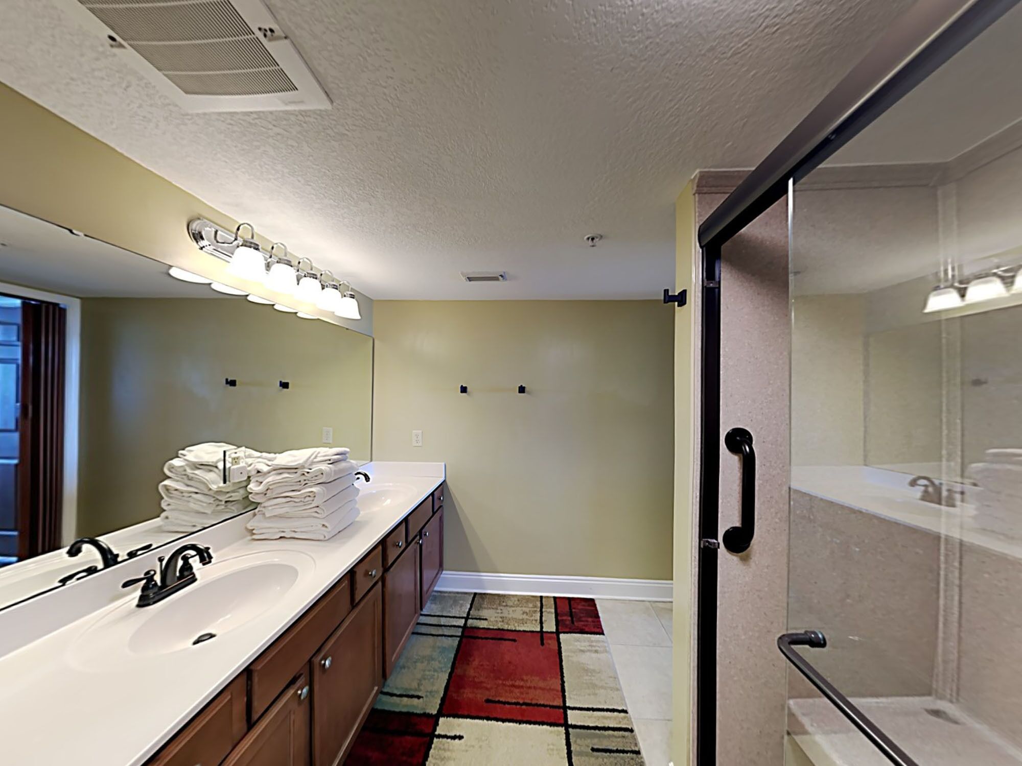 A modern bathroom with a large mirror, dual sinks, and a shower area.