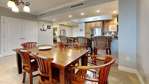 Un comedor con una mesa y sillas de madera, una araña y una cocina al fondo.