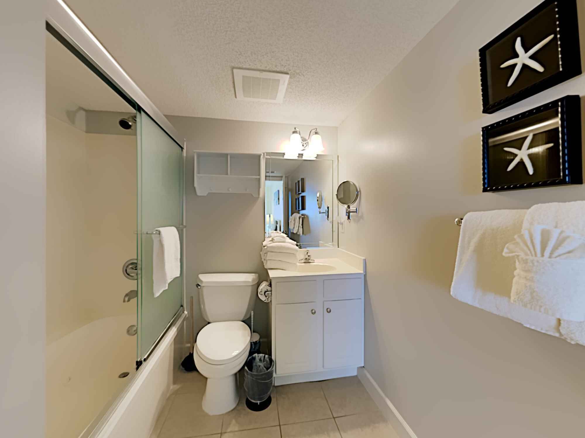 Ein Badezimmer mit Duschkabine aus Glas, Toilette, Waschbecken mit Waschtisch und zwei Seestern-Dekorationen an der Wand.