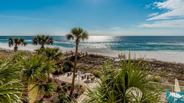A beach view with palm trees, a wooden fence, and a clear sky. - Sandy Key by Southern Vacation Rentals (Pensacola)