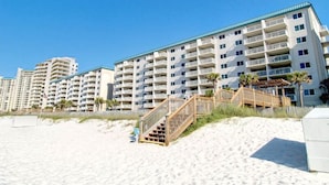A beachfront hotel with multiple floors, balconies, and a wooden staircase leading to the beach. - Sandy Key by Southern Vacation Rentals (Pensacola)