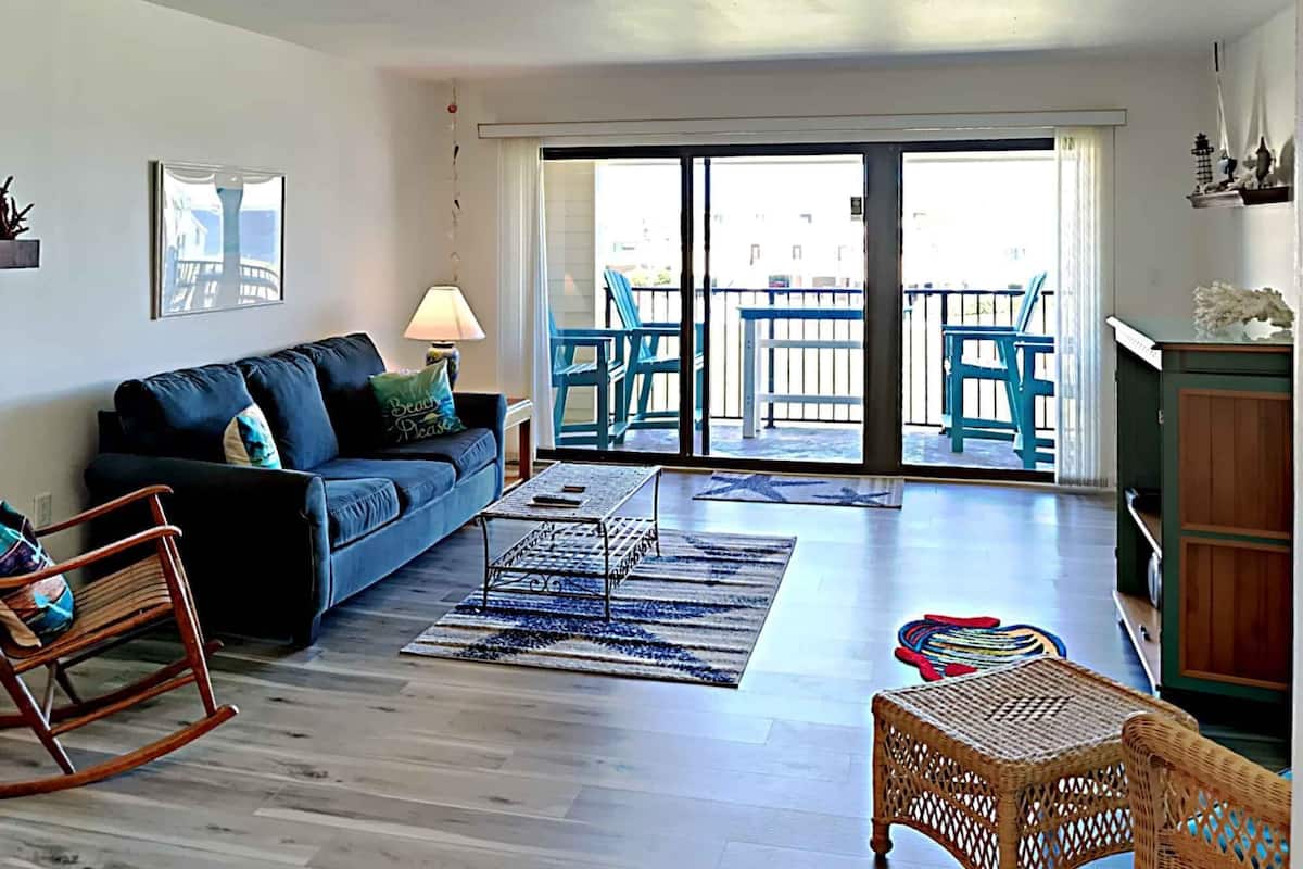 A living room with a sofa, a rocking chair, a coffee table, and a balcony with chairs.