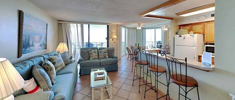 A living room with a sofa, a coffee table, and a dining area with bar stools.
