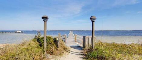 A sandy beach path leading to the sea with two lamp posts on either side.