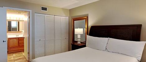 A bedroom with a bed, a nightstand, a mirror, and a closet.