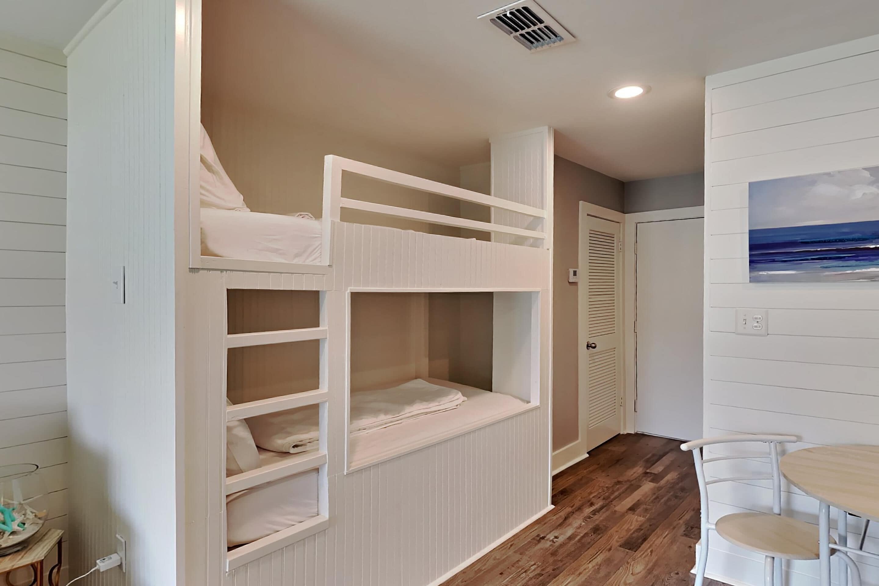 Une pièce avec un lit superposé, une petite table avec des chaises et un tableau accroché au mur.