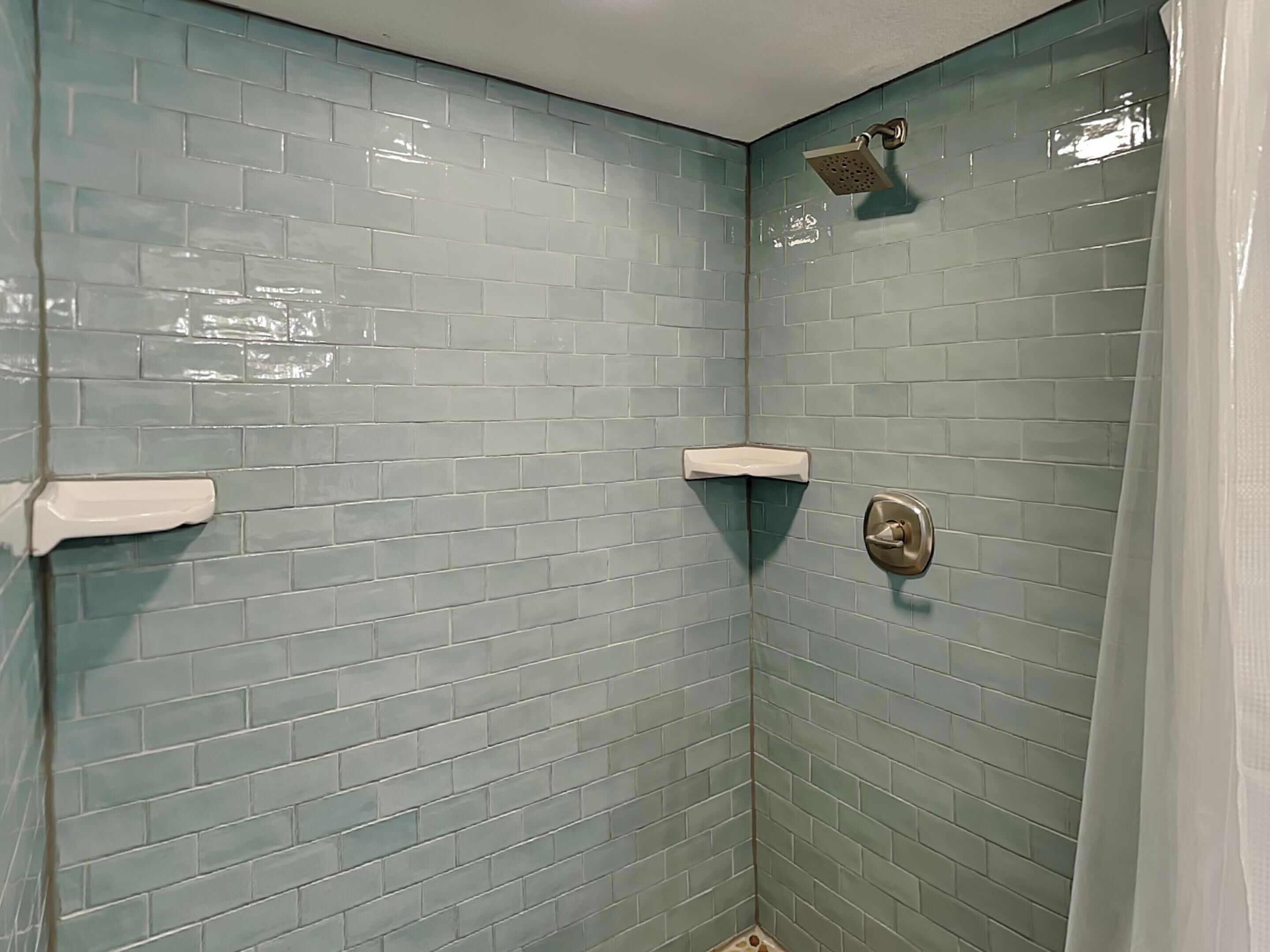 Casa de banho com paredes azulejadas em azul claro, um chuveiro e um rolo de papel higiénico.