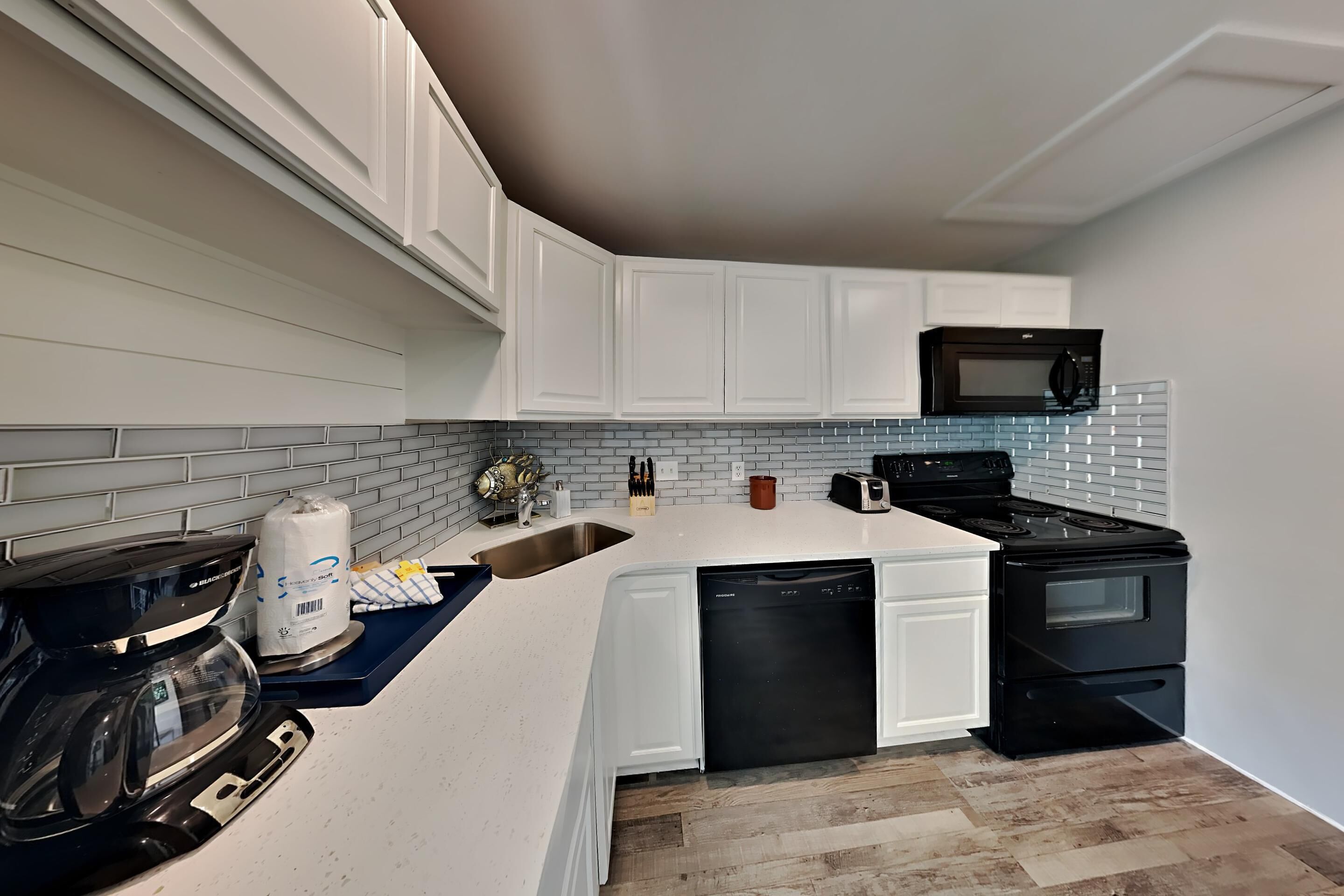 A modern kitchen with white cabinets, a black stove, a microwave, and a coffee maker.