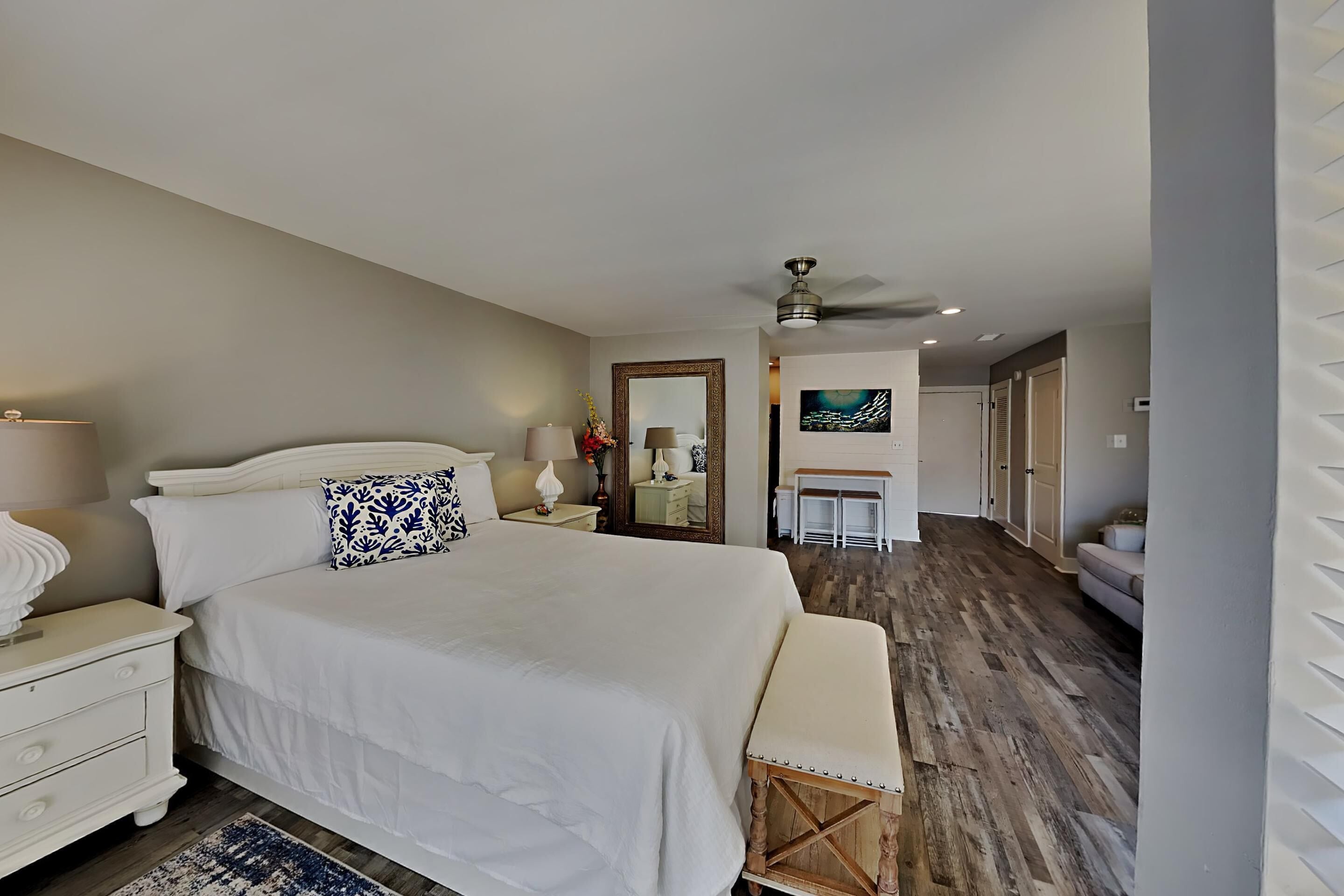 A bedroom with a large bed, bedside tables, a mirror, and a ceiling fan.