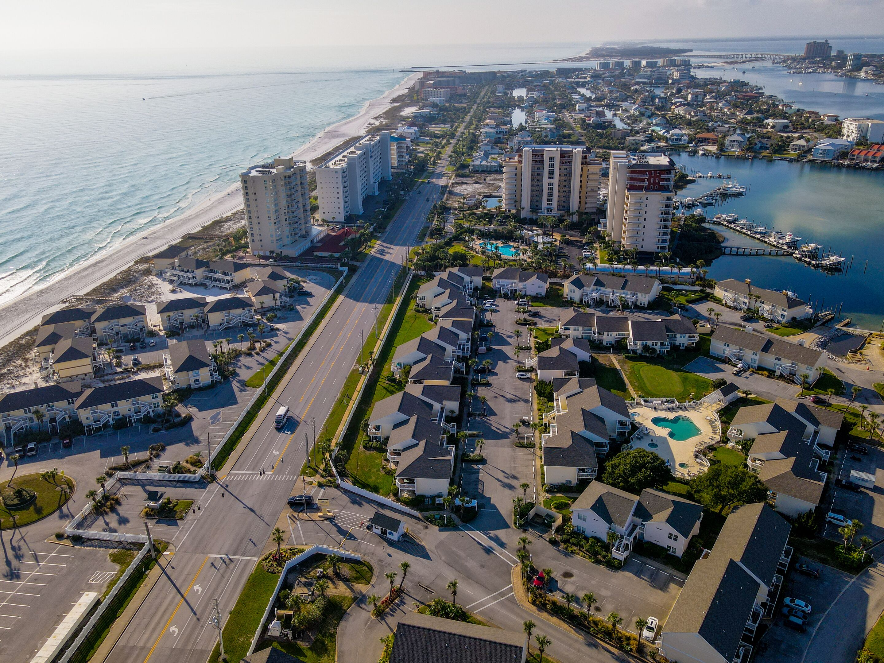 Vista aérea de uma área residencial costeira com propriedades à beira-mar, um porto de iates e uma estrada que leva à praia.