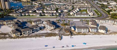 An aerial view of a coastal residential area with beachfront properties, a marina, and a road leading to the beach.