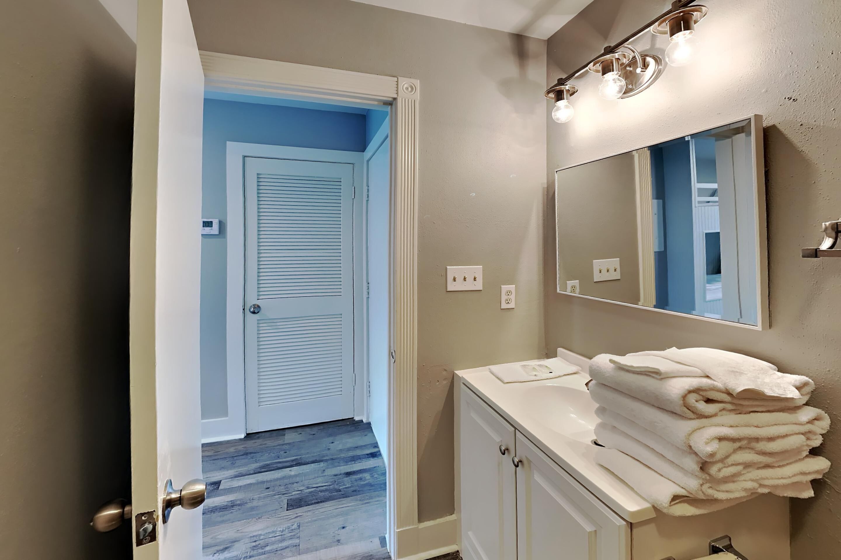 A bathroom with a white vanity, a mirror, and a stack of towels.
