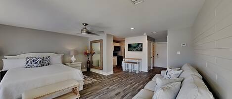 A modern bedroom with a large bed, a bench, a sofa, and a dining area.