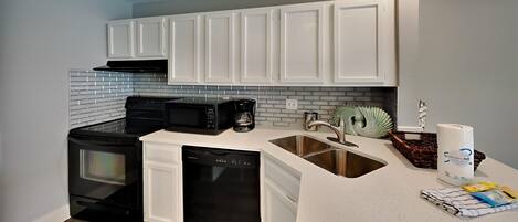 A compact kitchen with white cabinets, a black stove, and a dishwasher.