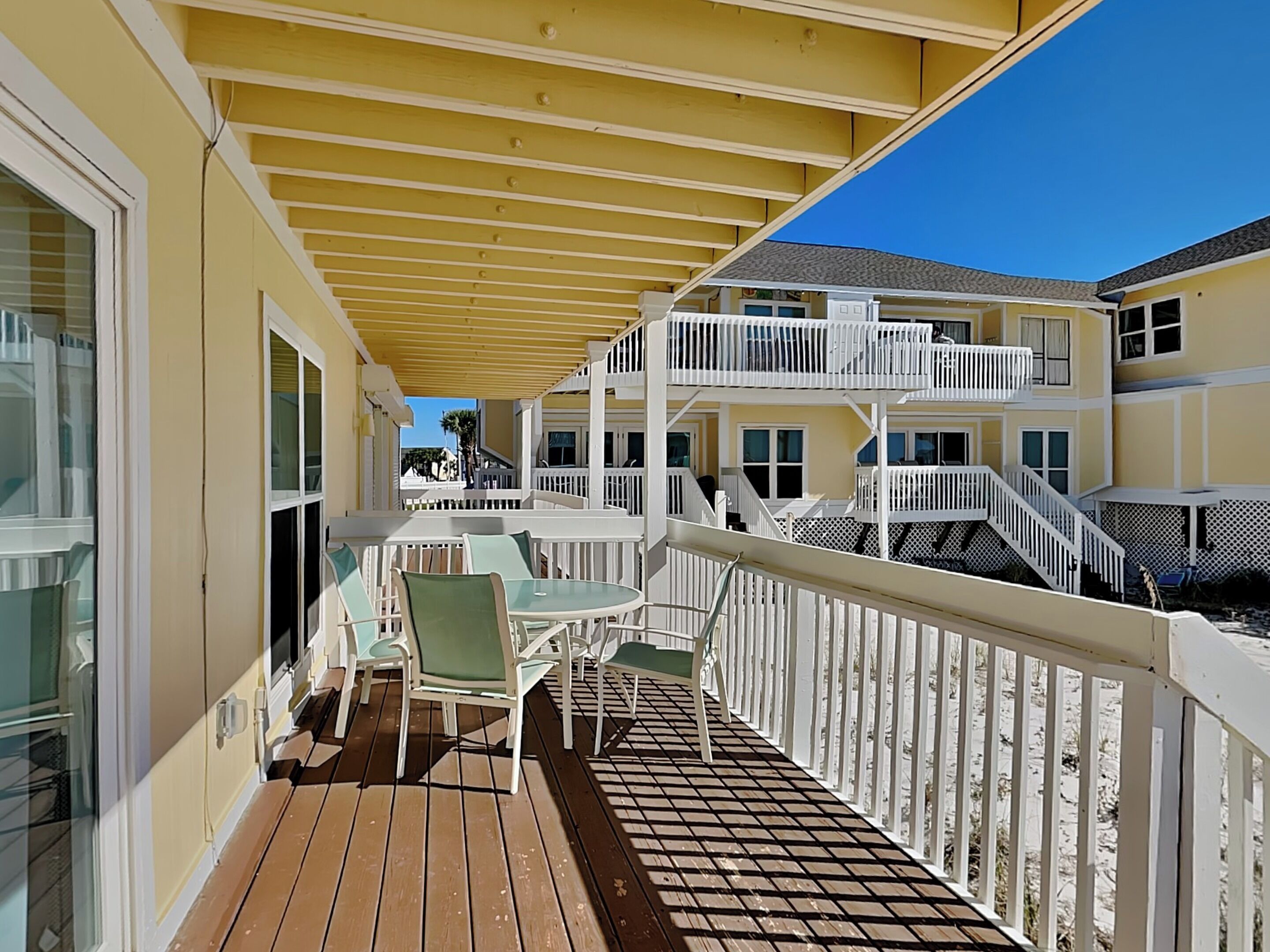 A wooden deck with outdoor furniture and a covered area, overlooking a multi-story building with balconies.