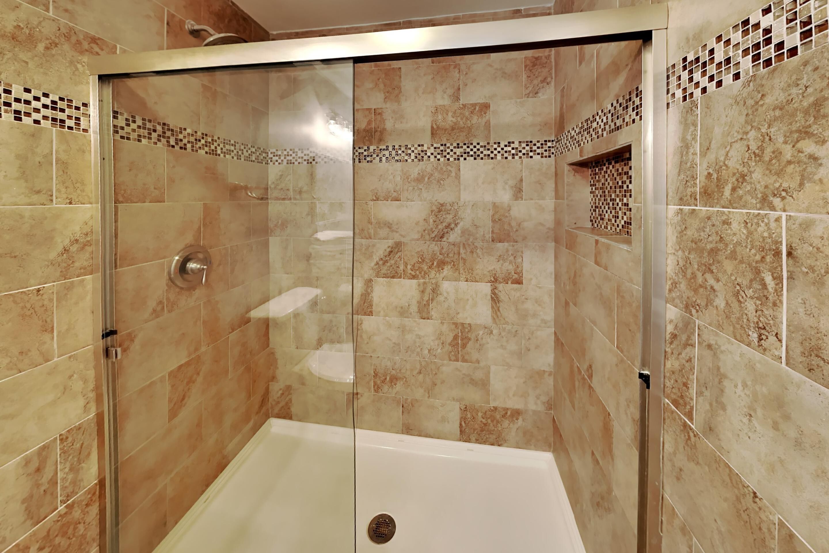 A glass-enclosed shower area with beige tiles and a white bathtub.