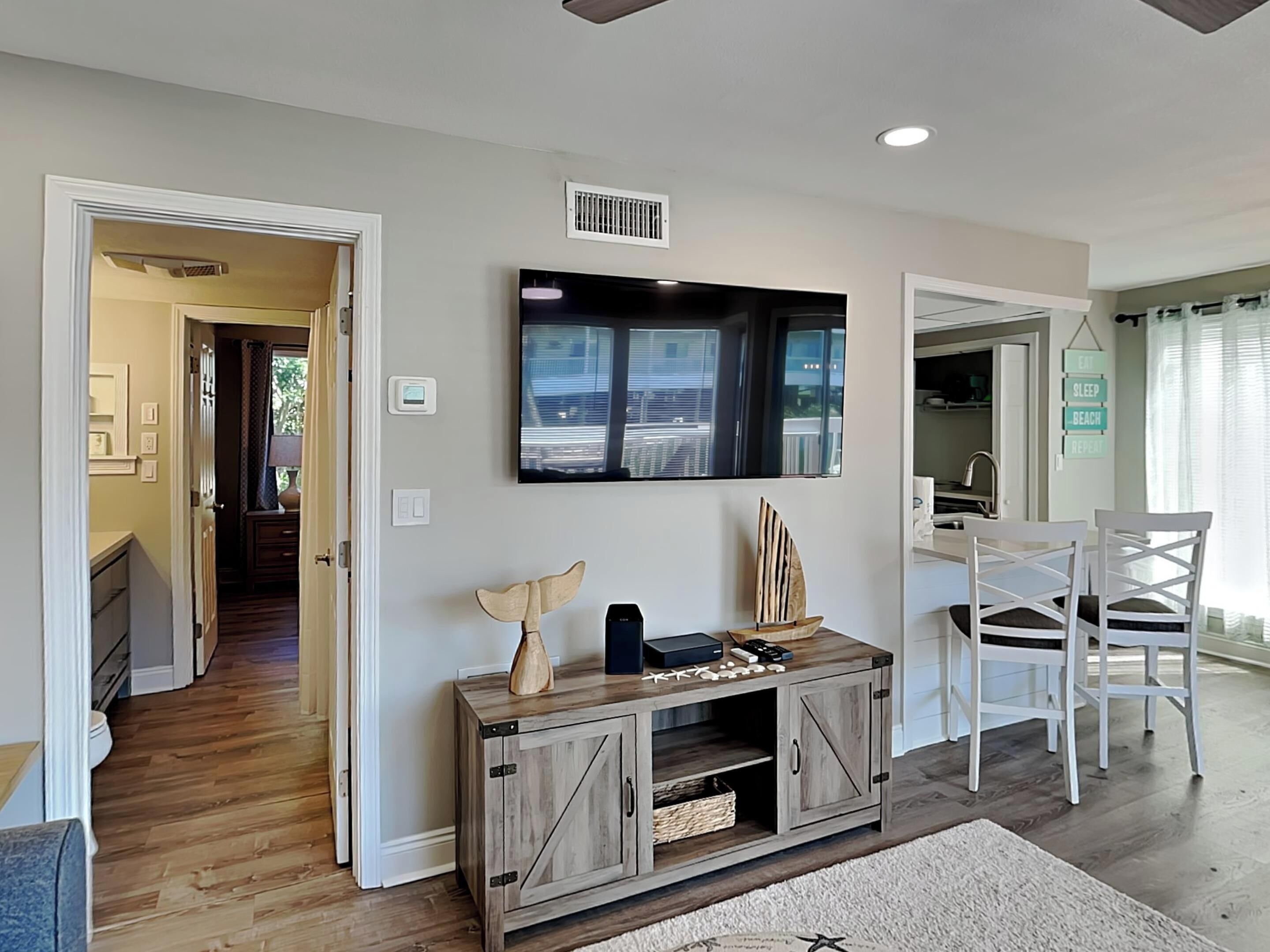 A modern living room with a wooden cabinet, a mounted TV, and a dining area with white chairs.