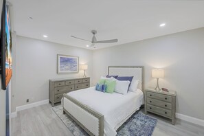 A bedroom with a bed, nightstands, a ceiling fan, and a painting on the wall.