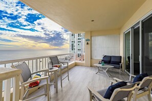 A balcony with a view of the ocean, furnished with chairs and a table, and a sliding glass door.