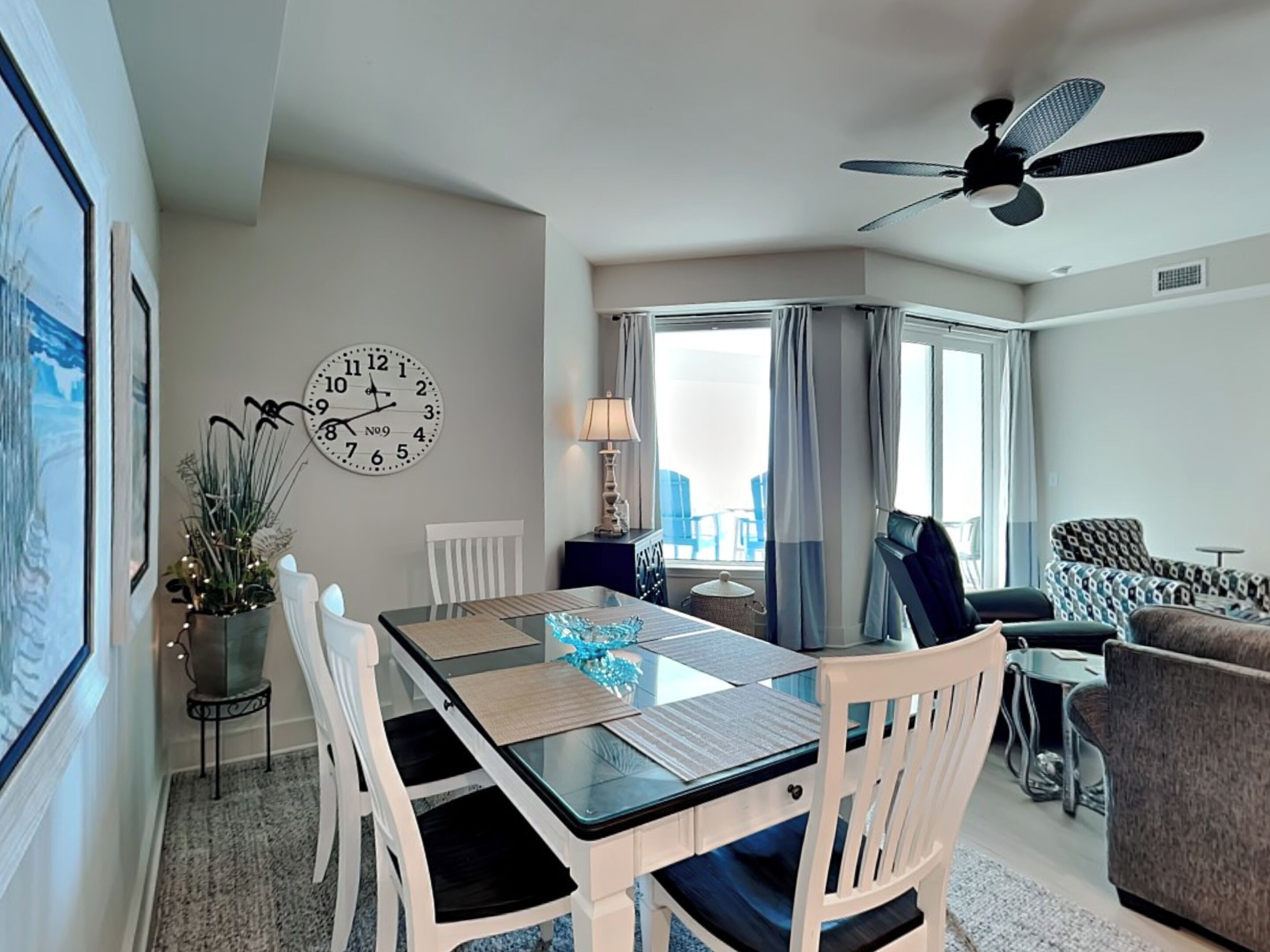 Una sala de estar moderna con comedor, ventilador de techo, un reloj grande y vistas al exterior.