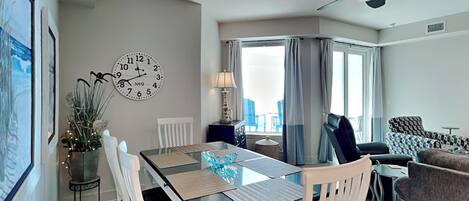 Una sala de estar moderna con comedor, ventilador de techo, un reloj grande y vistas al exterior.