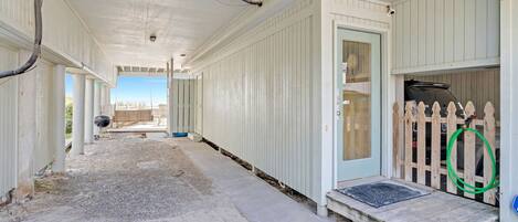 A covered porch with a concrete floor, a wooden fence, and a door leading to a garage.