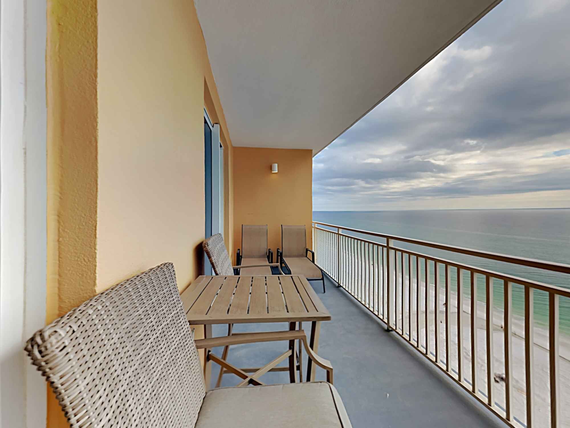 A balcony with a wooden table and chairs, a wicker sofa, and a view of the sea.