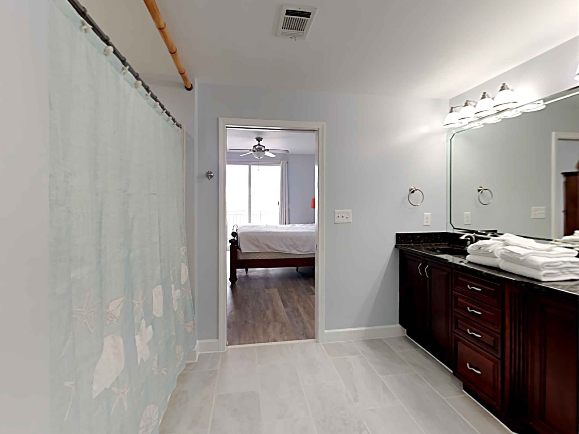 A bedroom with a bed, a bathroom with a vanity and mirror, and a hallway leading to another room.