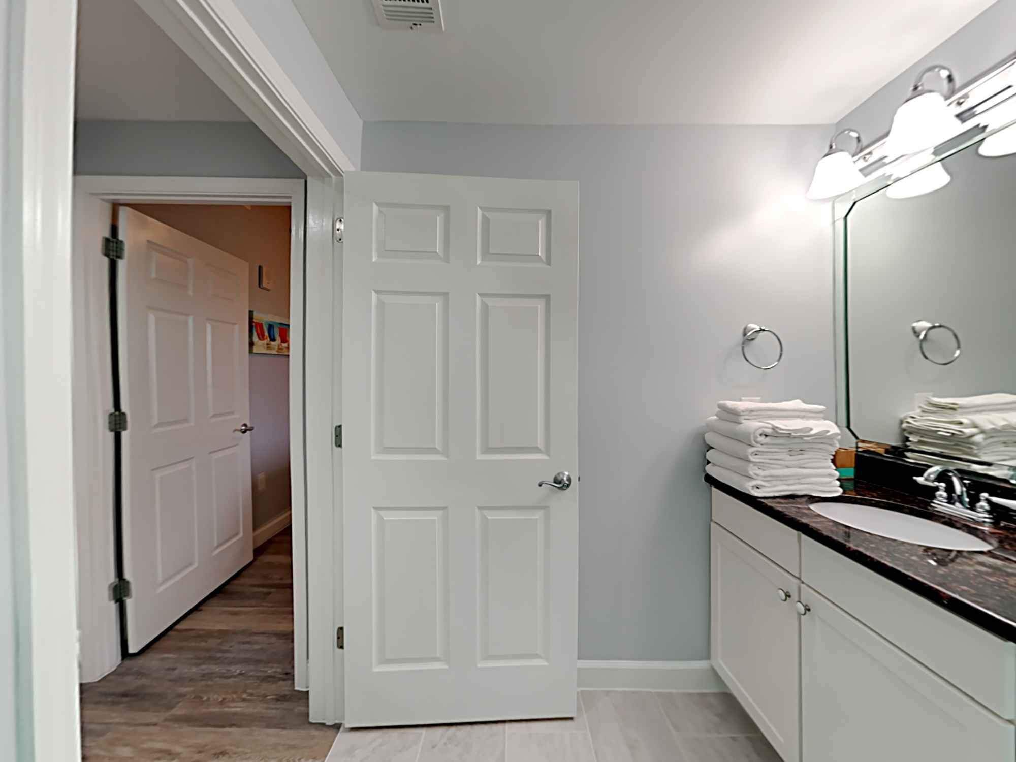 A bathroom with a white door, a vanity with a mirror, and a sink.