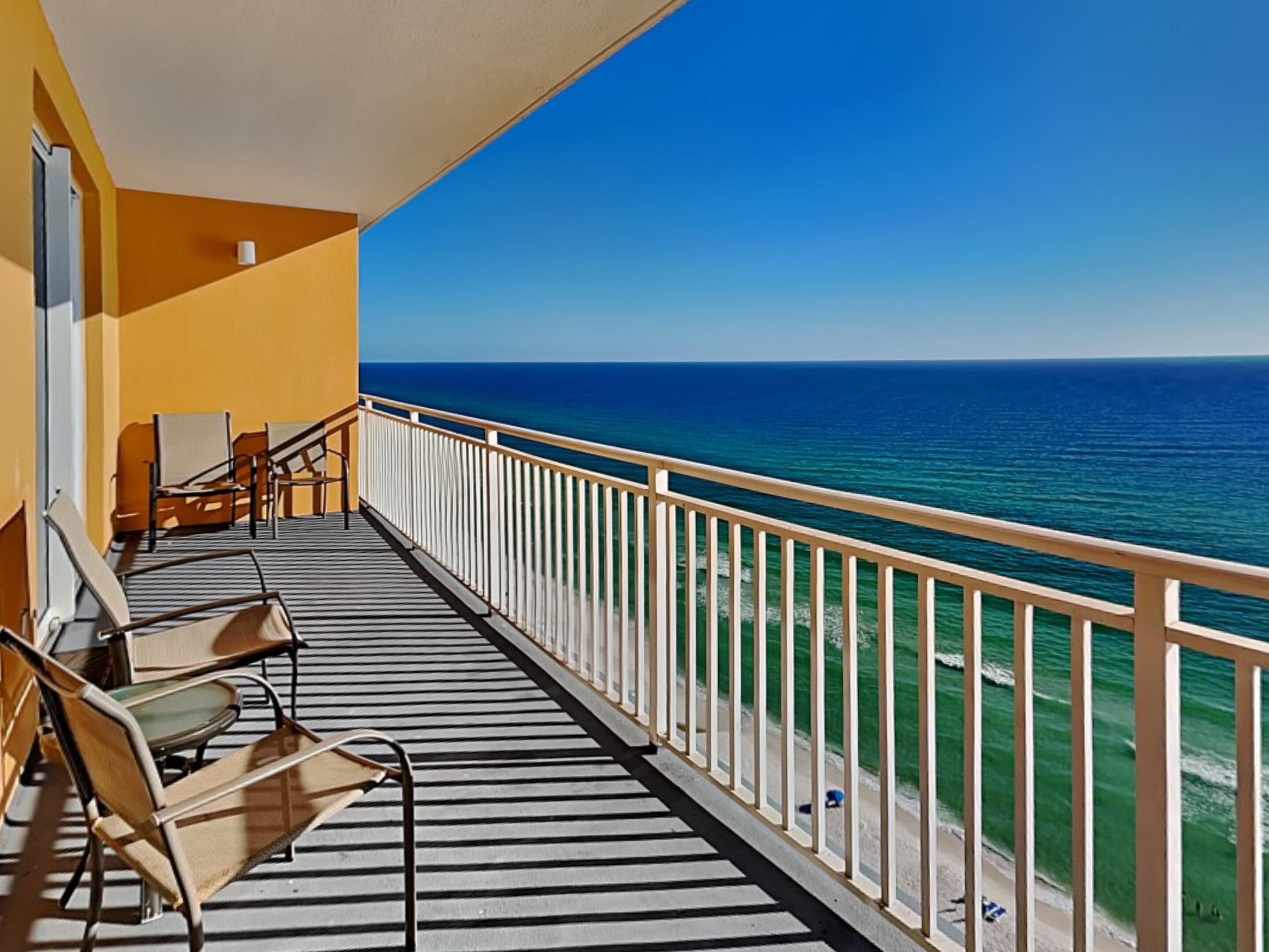 A balcony with a view of the ocean, featuring a railing and a few chairs.