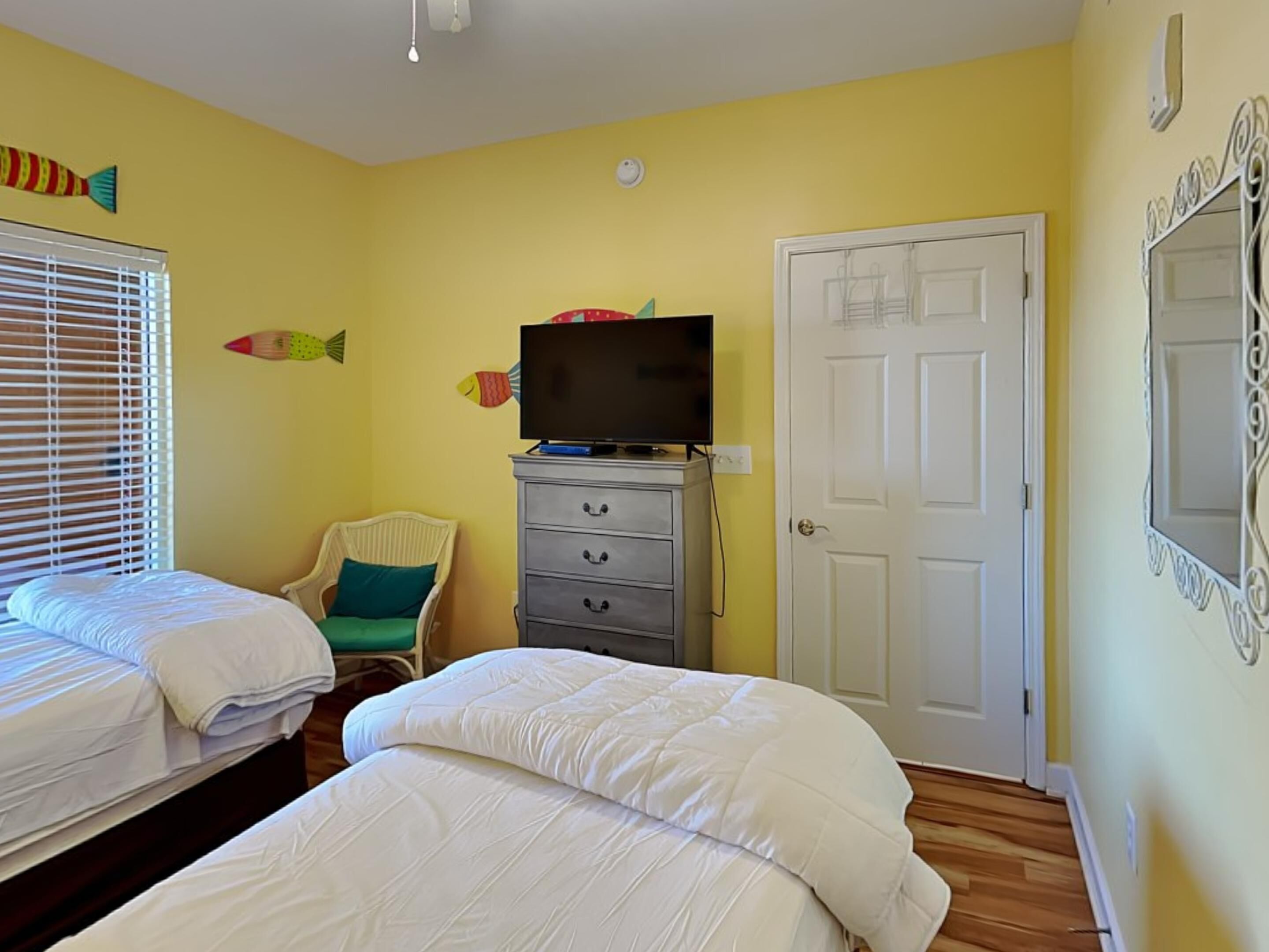 Un dormitorio con dos camas, un televisor sobre un tocador y una puerta con un espejo.